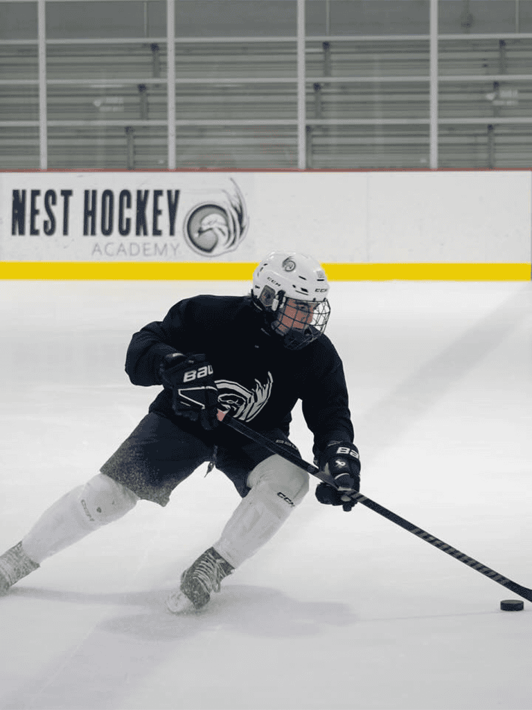 Young hockey player in black jersey on ice rink practicing skating and puck control at Nest Hockey Academy.