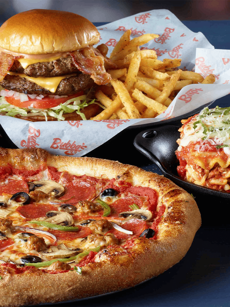 Juicy cheeseburger with bacon, fries, and classic pizza with toppings on a black tray.