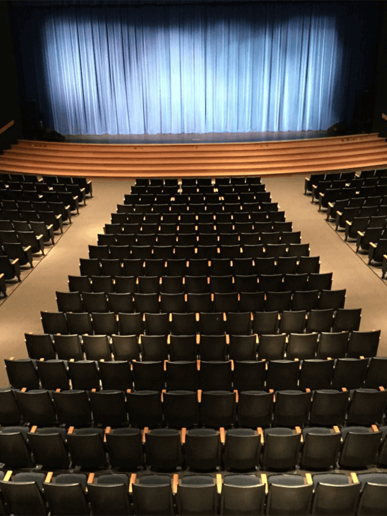 Auditorium with stage, seating, and blue curtain for events and performances.