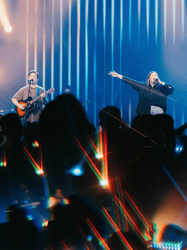 Live music concert featuring performers with guitars on stage and vibrant light effects.