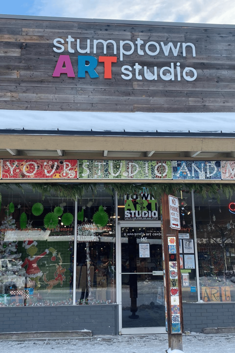 Colorful art studio storefront in Stumptown with vibrant mosaic signs and holiday decorations.