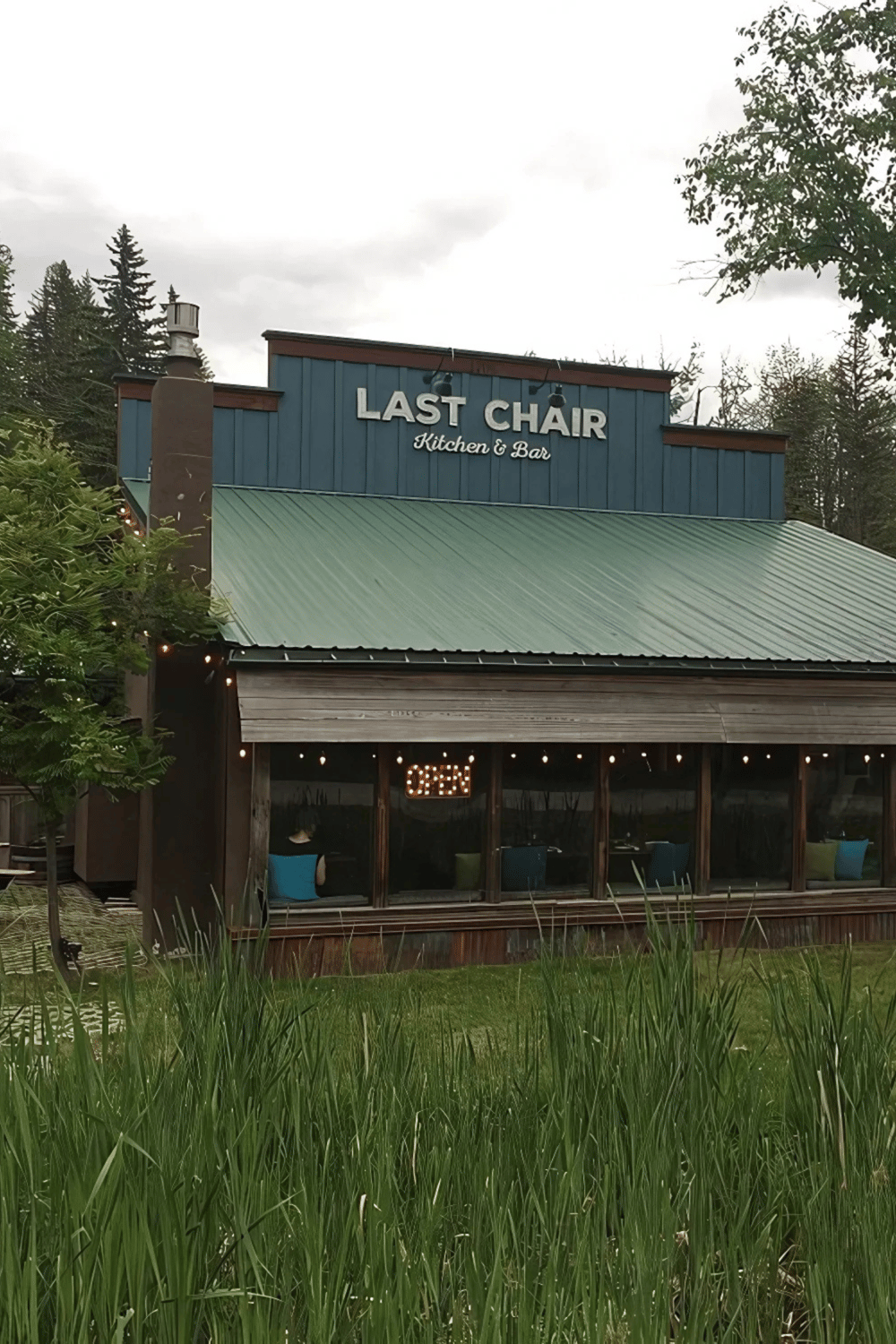 Cozy restaurant exterior with "Last Chair Kitchen & Bar" sign in a natural setting.