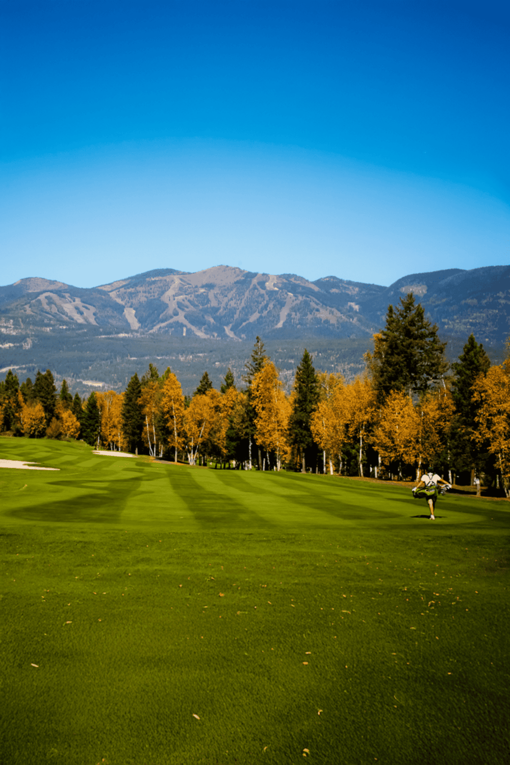 Vibrant golf course with mountain backdrop and fall foliage, perfect for outdoor sports and nature enthusiasts.