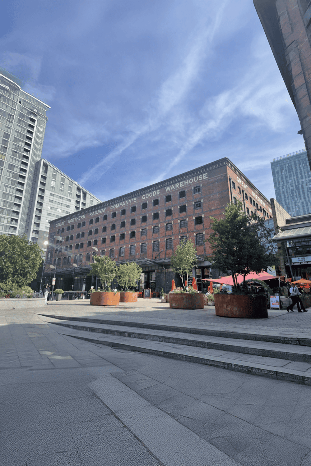 Historic warehouse building with modern cityscape, outdoor seating, and pedestrian area.