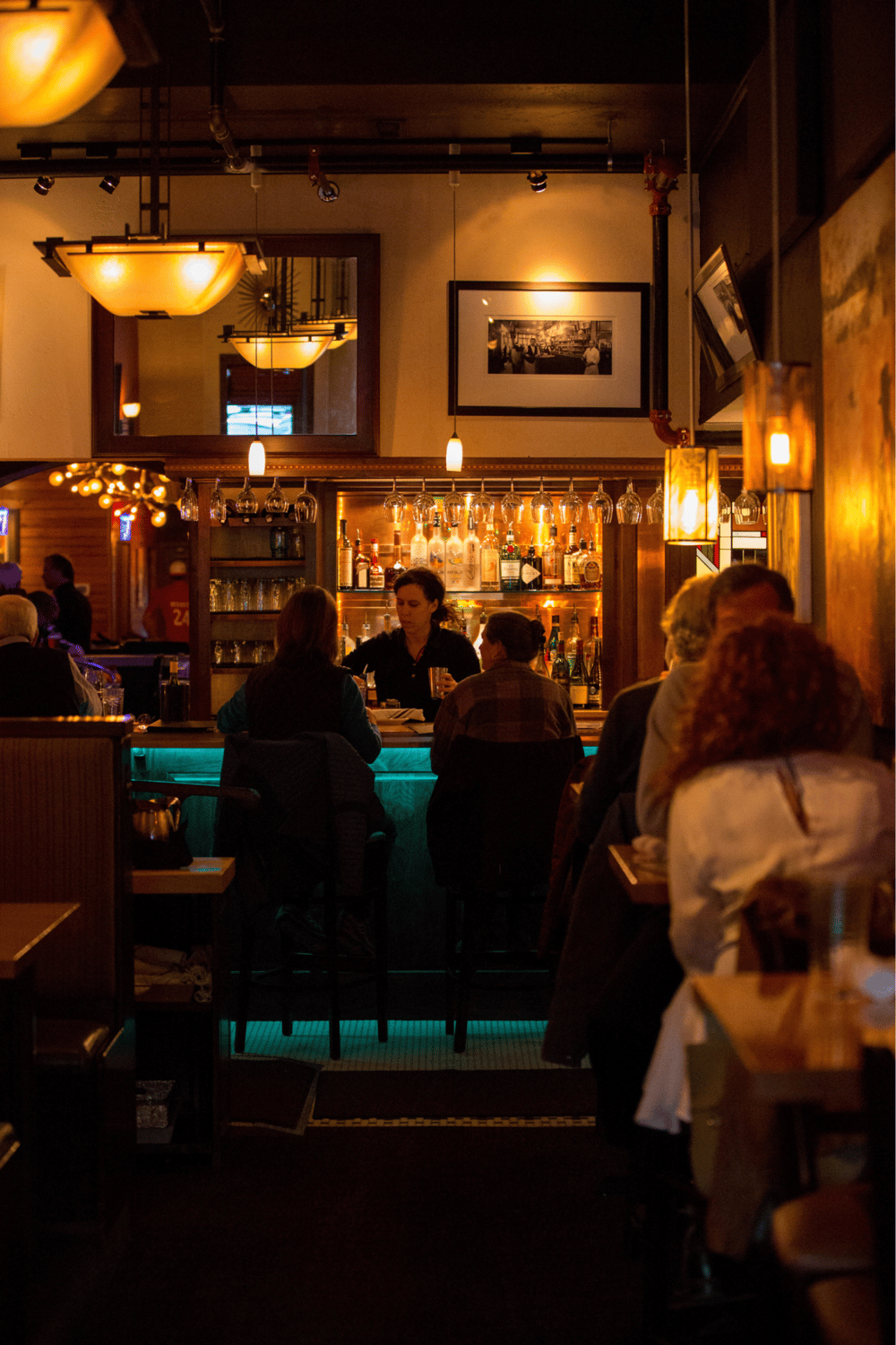 Relaxed bar scene inside a cozy restaurant with warm lighting and patrons enjoying drinks.