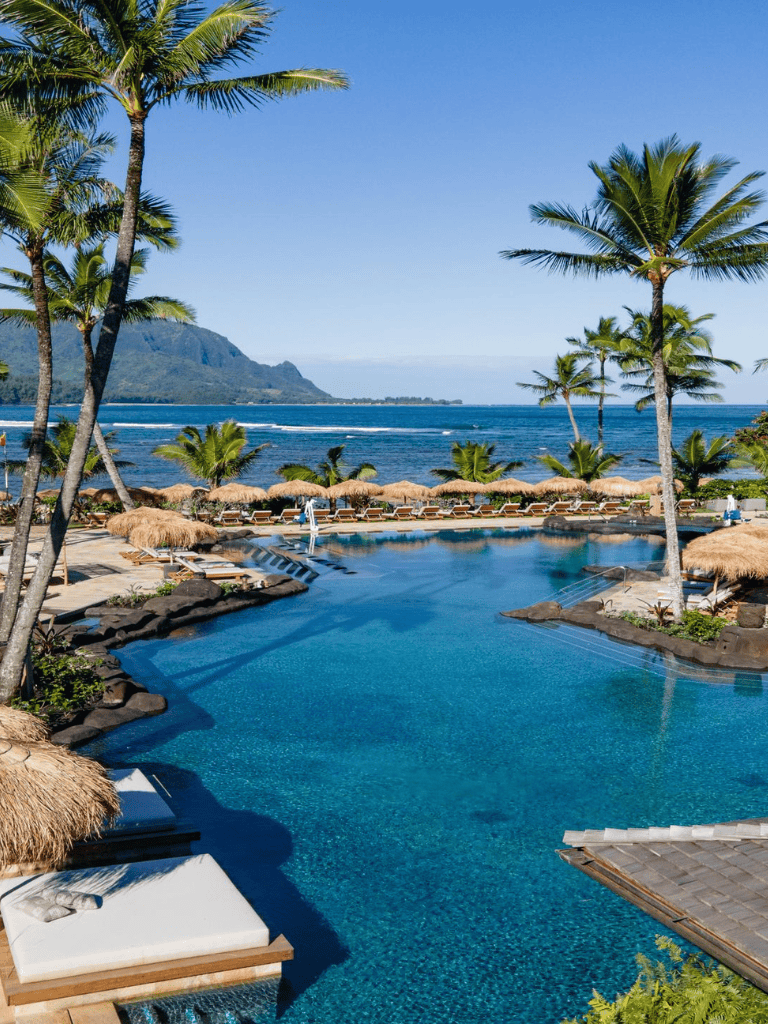 Relaxing oceanfront resort with infinity pool, palm trees, and mountain view in tropical paradise.