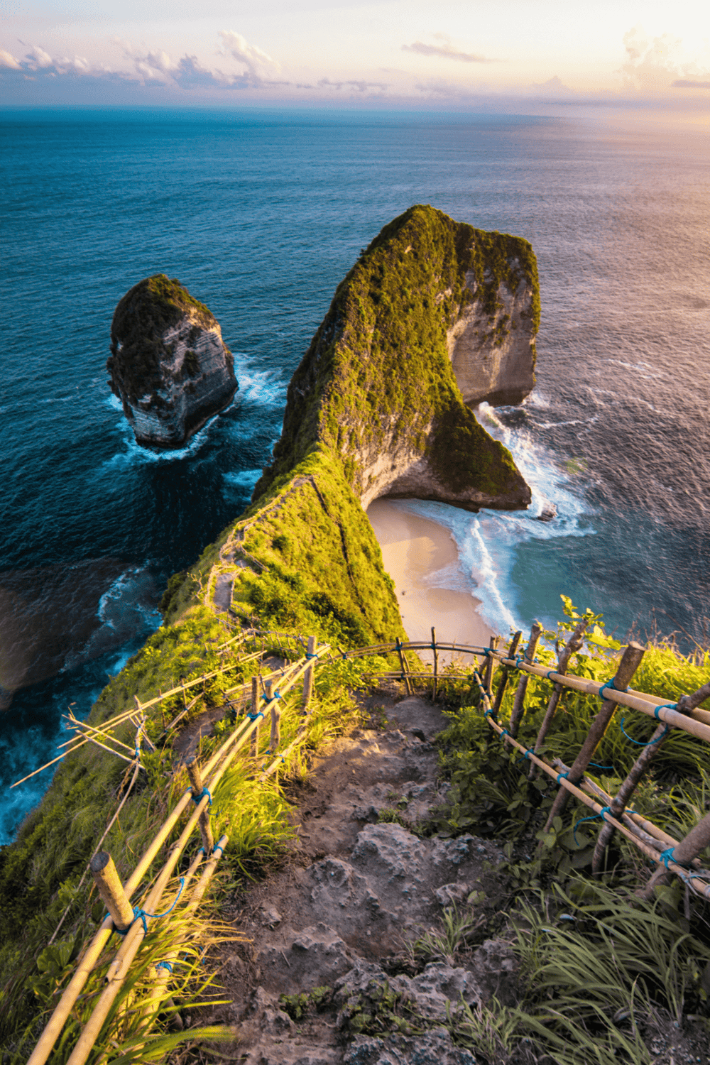 Breathtaking view of Bali's iconic cliffs, lush greenery, and secluded beach cove at sunset.