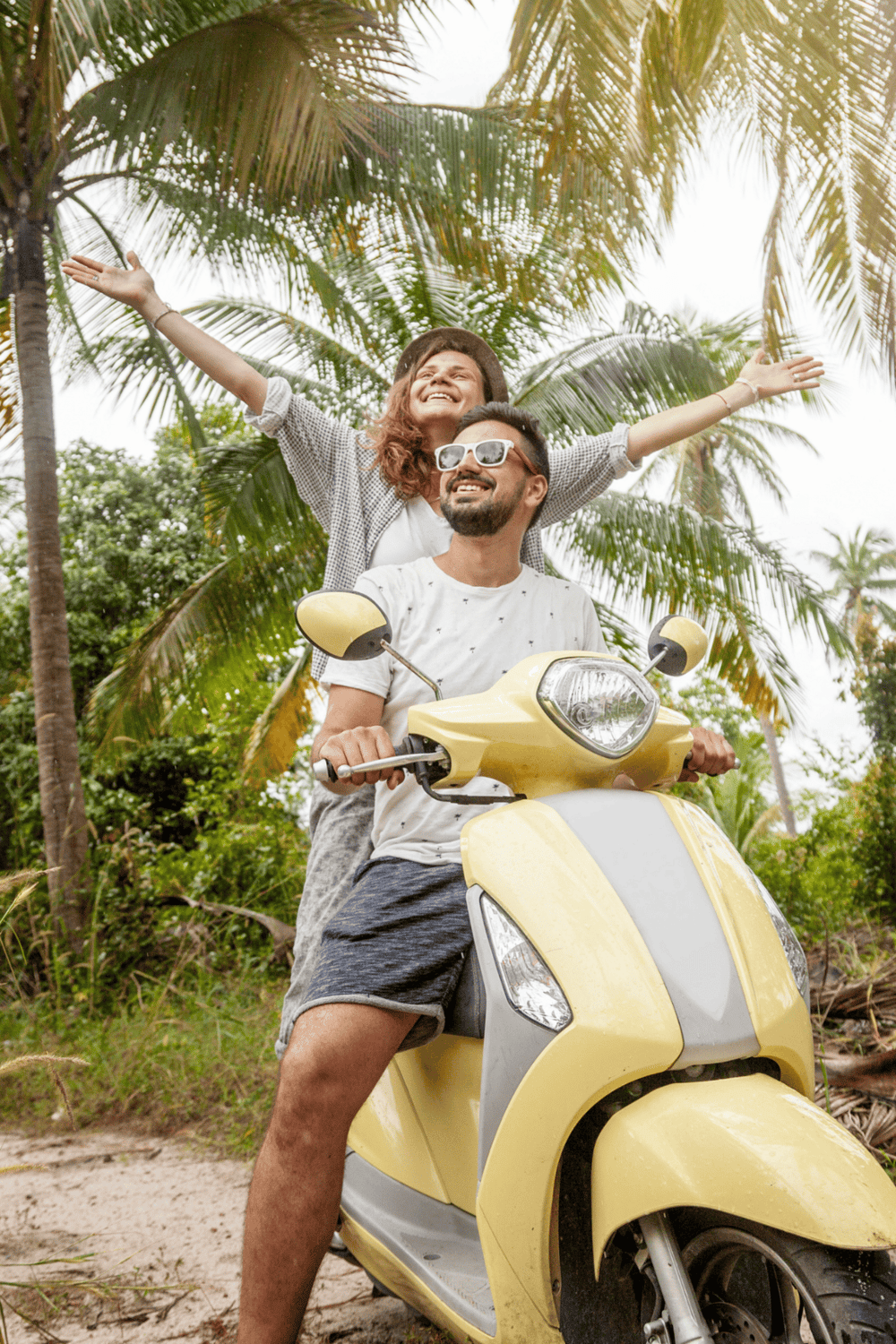 Joyful couple riding yellow scooter in tropical palm forest for travel adventure.