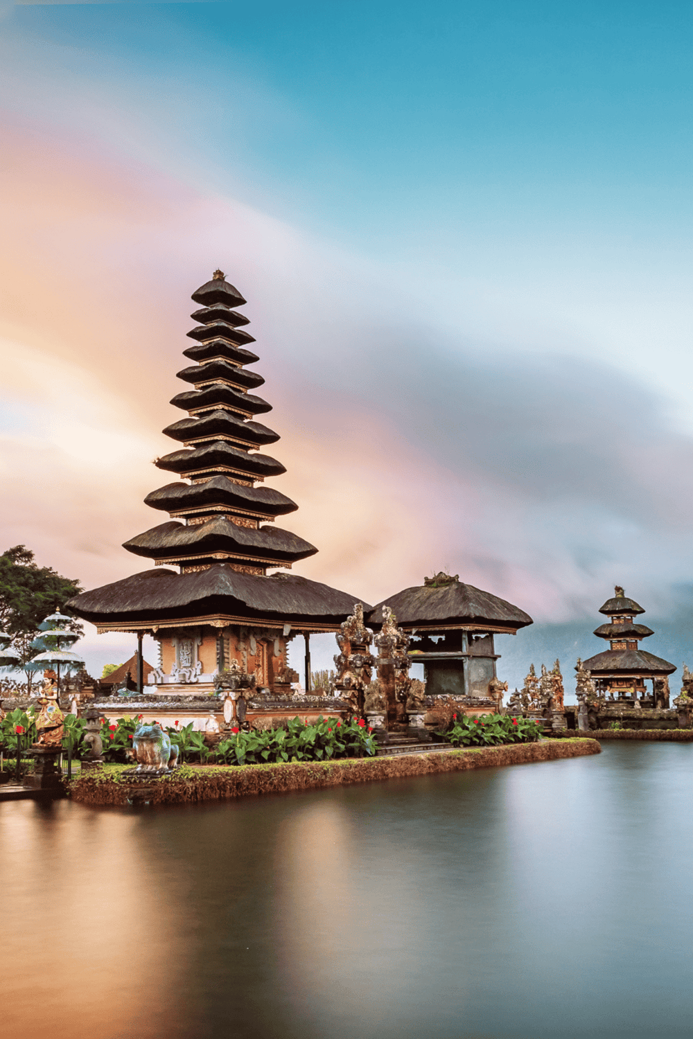 Traditional Balinese temple with multi-tiered pagoda on a lake at sunset, showcasing cultural and spiritual heritage.