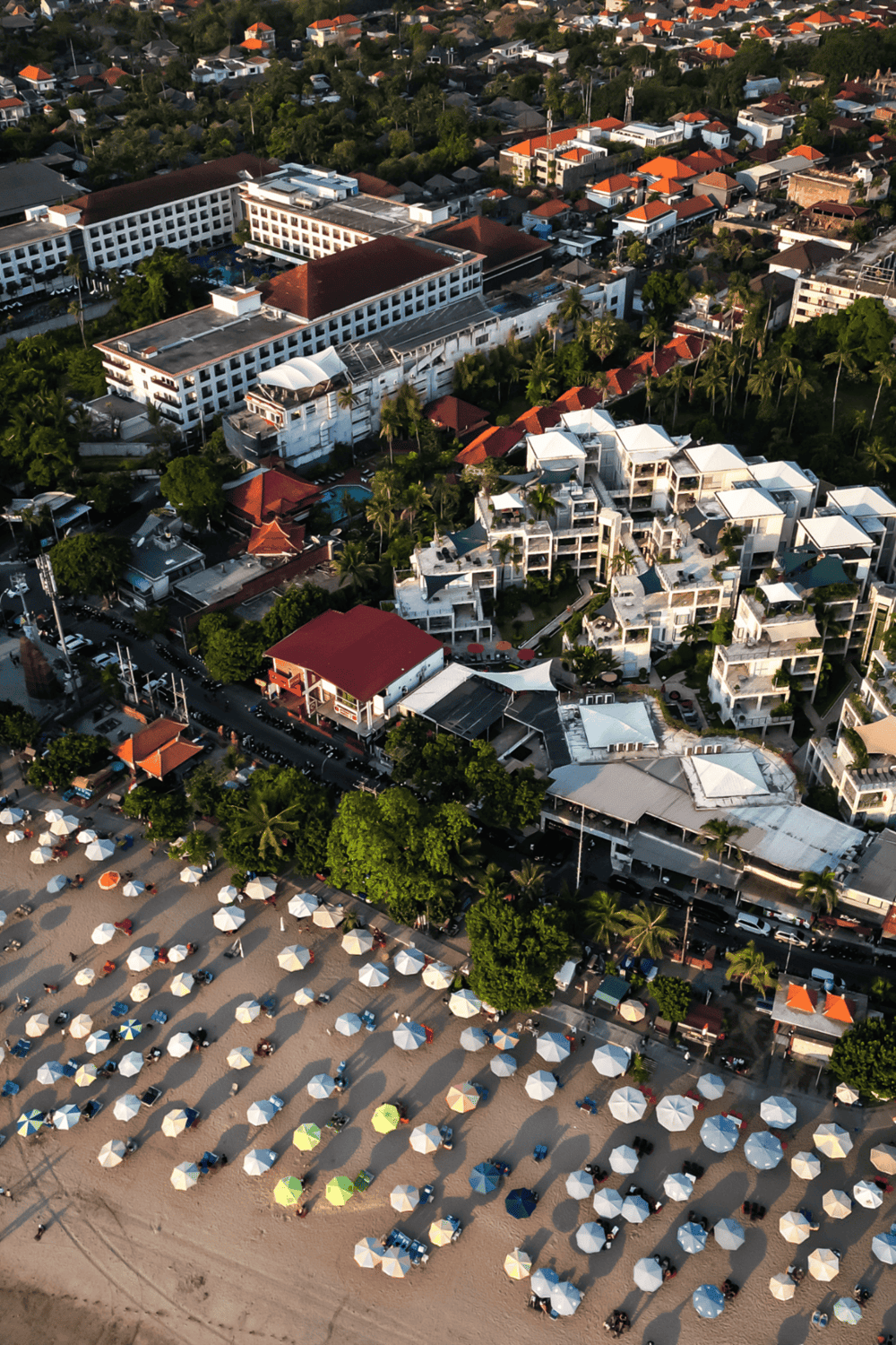 Vibrant beach resort with white umbrellas, colorful lounge chairs, and luxury hotels surrounded by lush greenery.