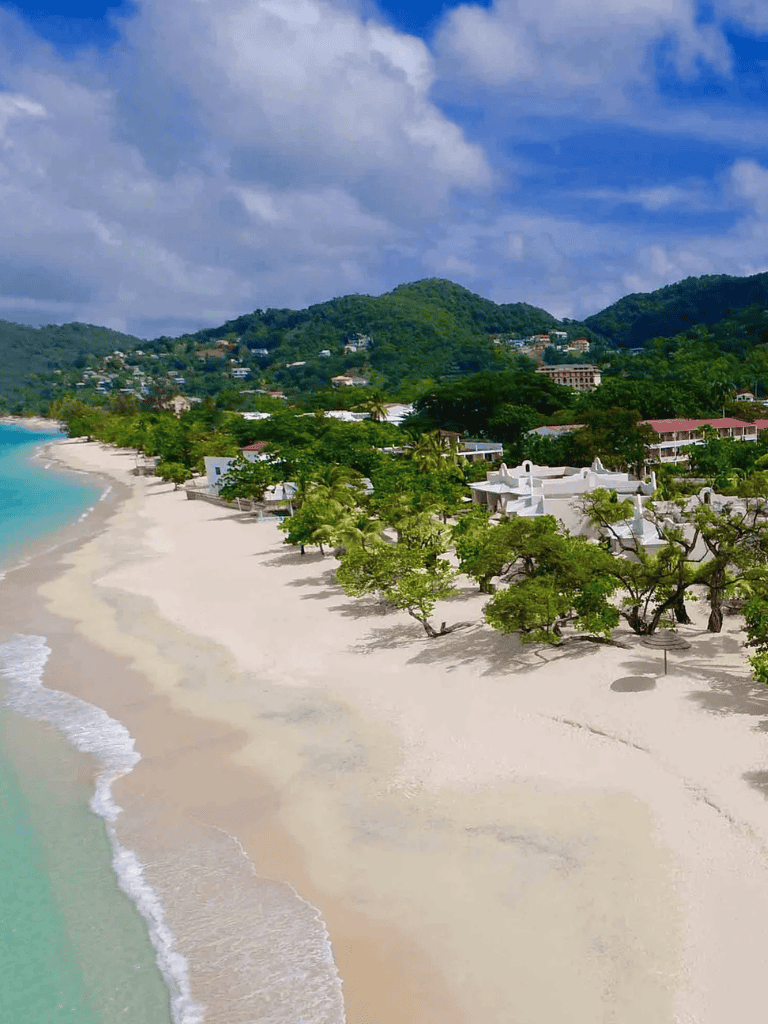 Pristine Caribbean beach with white sand, turquoise water, and lush green hills in the background.