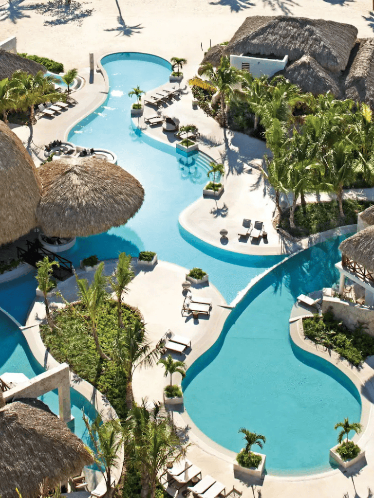 Stunning tropical pool with palm trees, lounge chairs, and thatched-roof cabanas at a luxury resort.