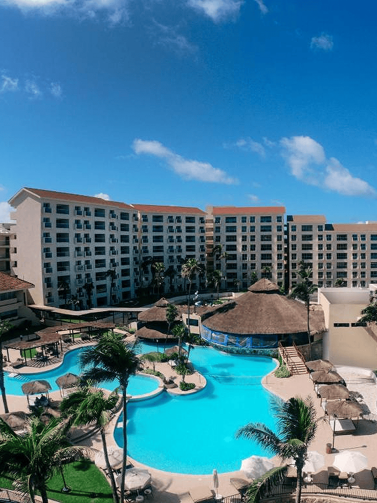 Relaxing resort pool with palm trees and sun umbrellas under a blue sky, perfect for vacation stays.
