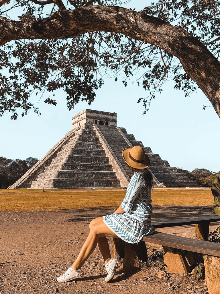 Ancient Mayan pyramid Tikal Guatemala with woman sitting on bench in hat and dress.