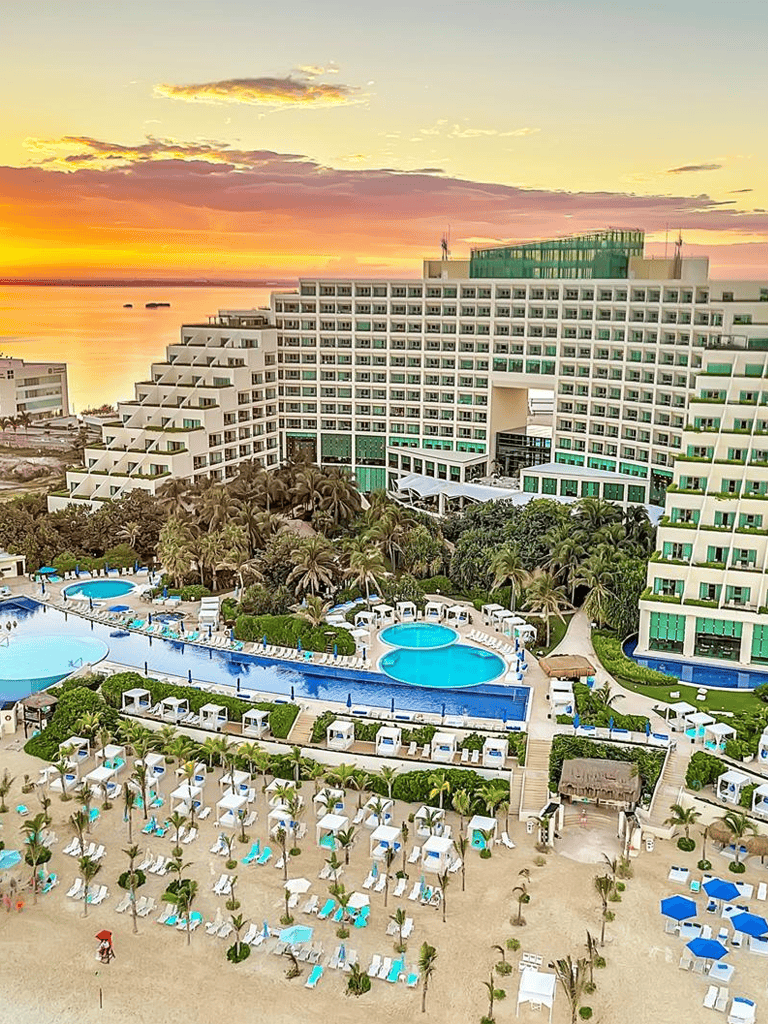 Luxurious beachfront hotel with pools, palm trees, and sunset view for ideal vacation stays.
