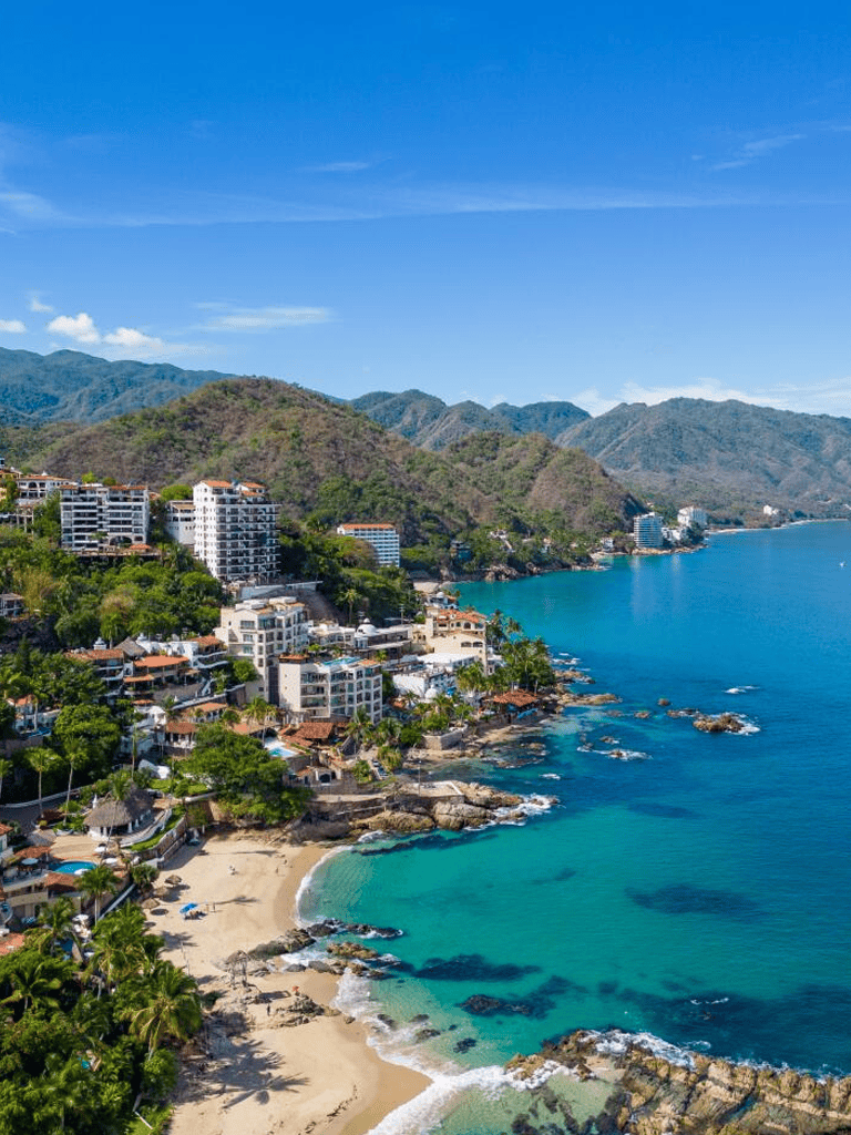 Stunning coastal view of luxury resorts and beach in Cabo San Lucas, Mexico, with lush mountains in background.