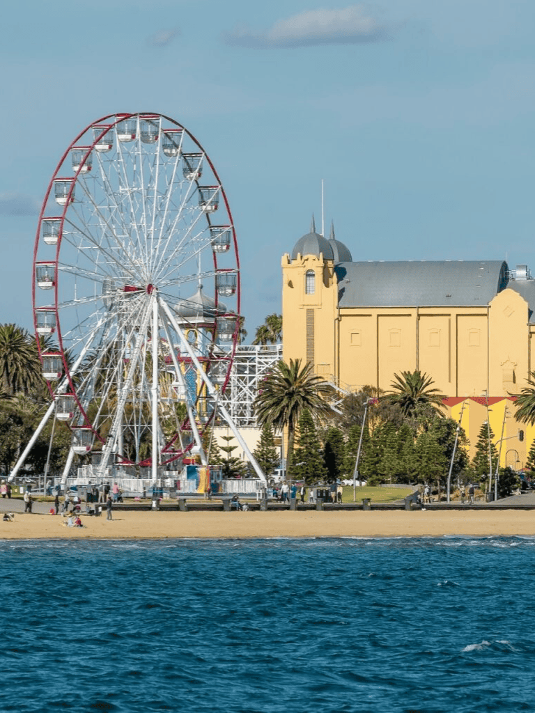 Colorful Ferris wheel at Santa Monica beach with historic building in background.