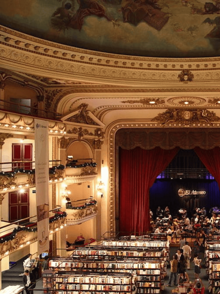 Elegant historic theater with ornate gold details and a busy book fair on stage and balcony levels.