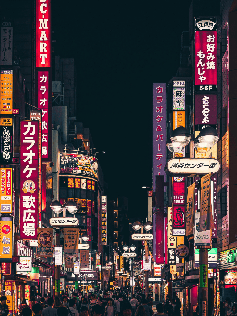 Bright neon cityscape at night in Tokyo with bustling crowds and vibrant advertising signs.