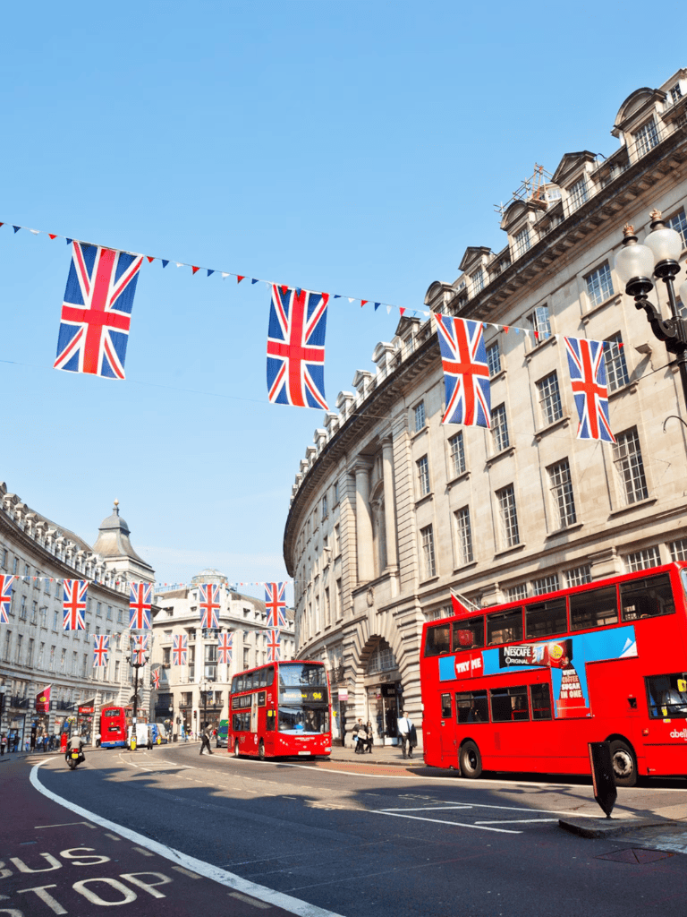 British flags and iconic double-decker buses on a busy London street, showcasing local landmarks and city atmosphere.