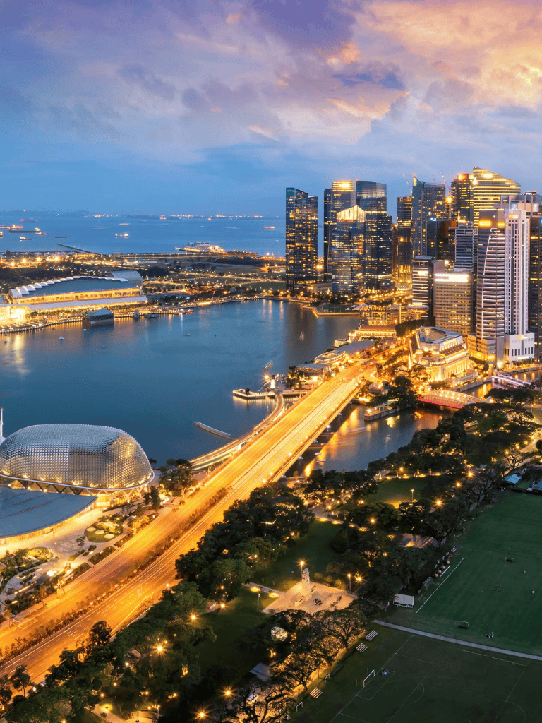 Bright Singapore city skyline at dusk with illuminated skyscrapers and waterfront view.