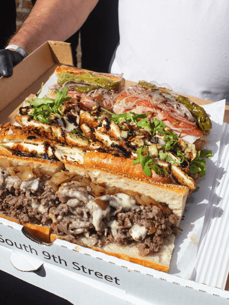 Cheesesteak sandwich with fresh toppings and melted cheese, served in a pizza box.