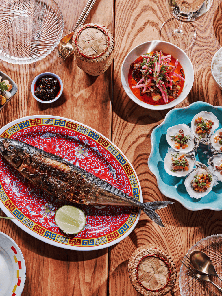 Fresh grilled fish on a colorful Asian-style plate with lime wedge, surrounded by various Asian dishes and dinnerware.