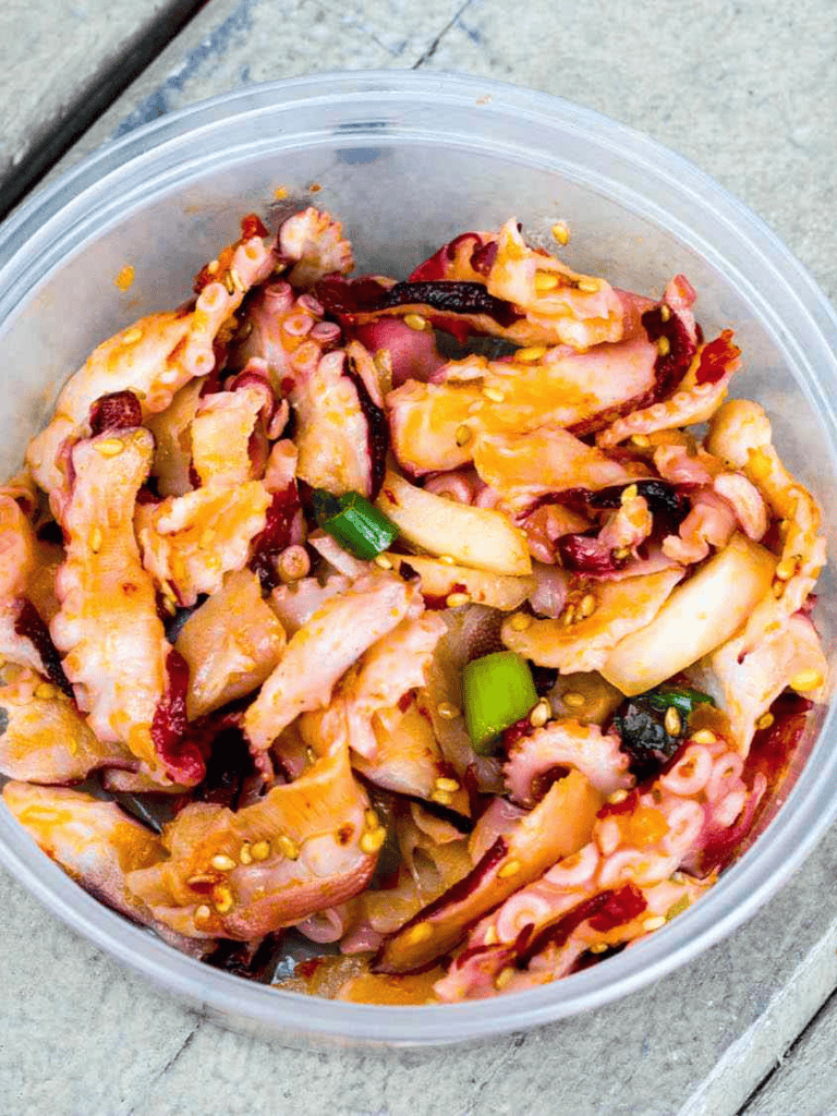 Raw marinated octopus with green onions in a plastic container, ready for cooking or presentation.