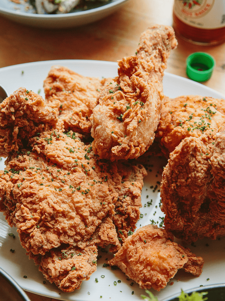 Crispy fried chicken drumsticks with golden-brown coating, garnished with chopped herbs.