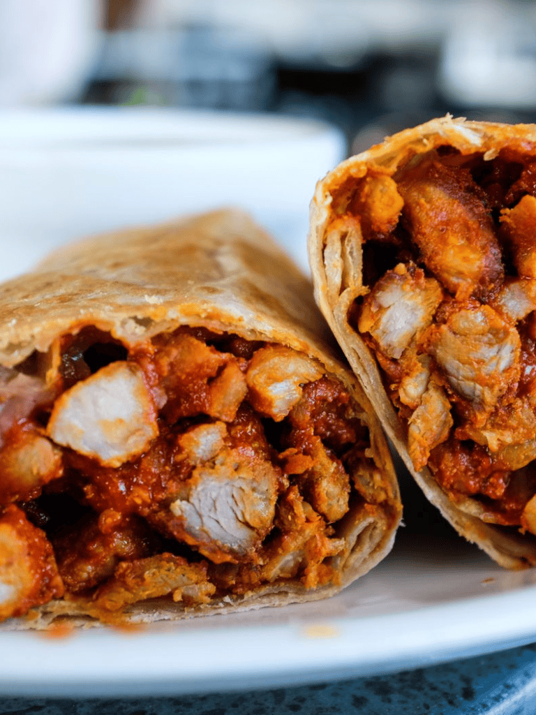 Creamy chicken burrito with spicy salsa and melted cheese on a white plate.