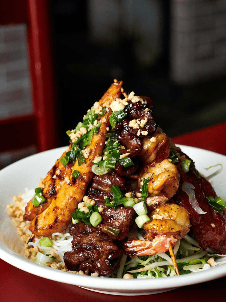 Grilled meat and seafood dish with green onions and chopped peanuts, served on a bed of noodles.