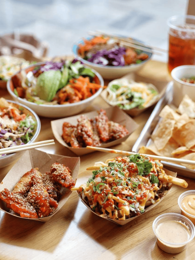 Spicy Asian fusion food platter with fries, skewers, and colorful salads for dining out or delivery.
