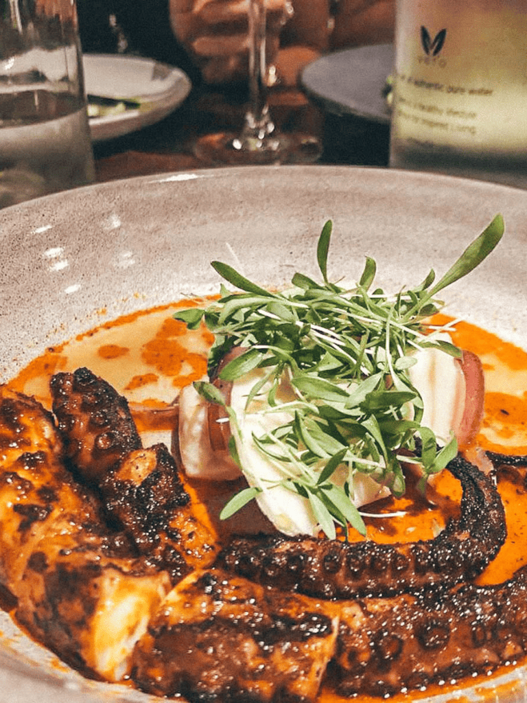 Fresh grilled octopus with herbs and creamy sauce, served with lemon for a delicious seafood dish.