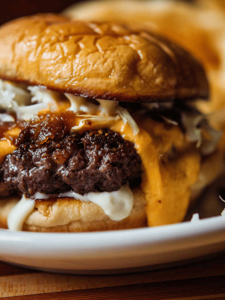 Juicy cheeseburger with melted cheese, crispy bun, and savory beef patty on a white plate.