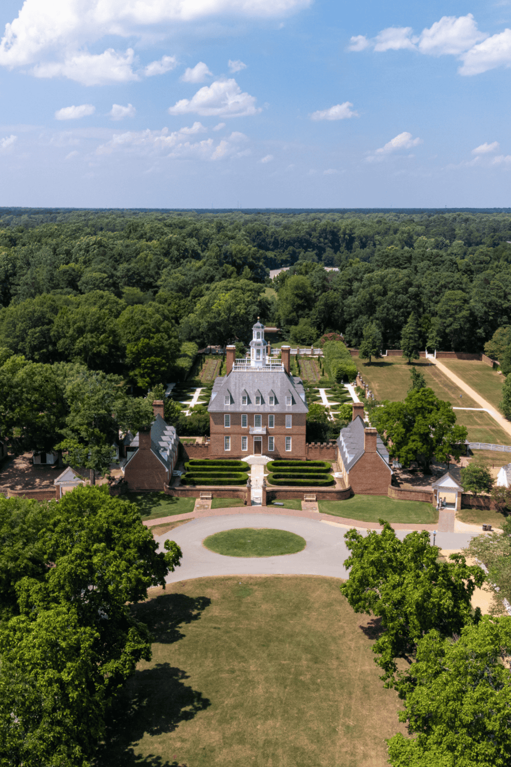Aerial view of historic estate with lush greenery, gardens, and classic architecture in scenic outdoor setting.