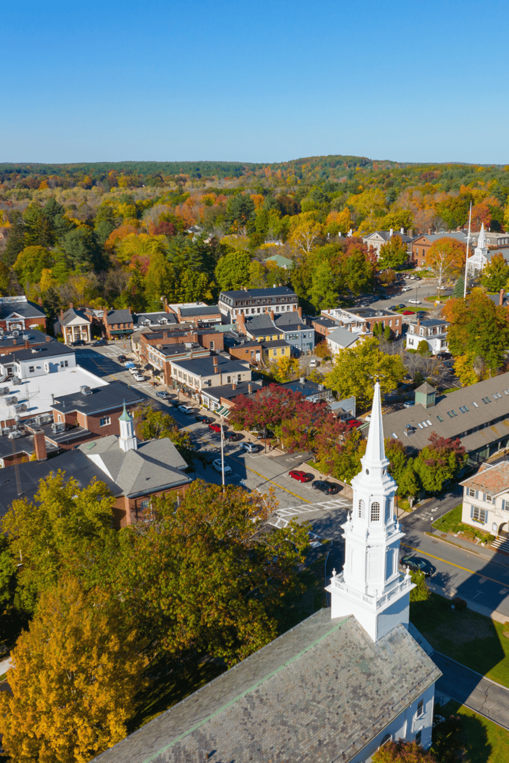 Colorful autumn town with church steeple and vibrant fall foliage, scenic views, local shops, and community atmosphere.