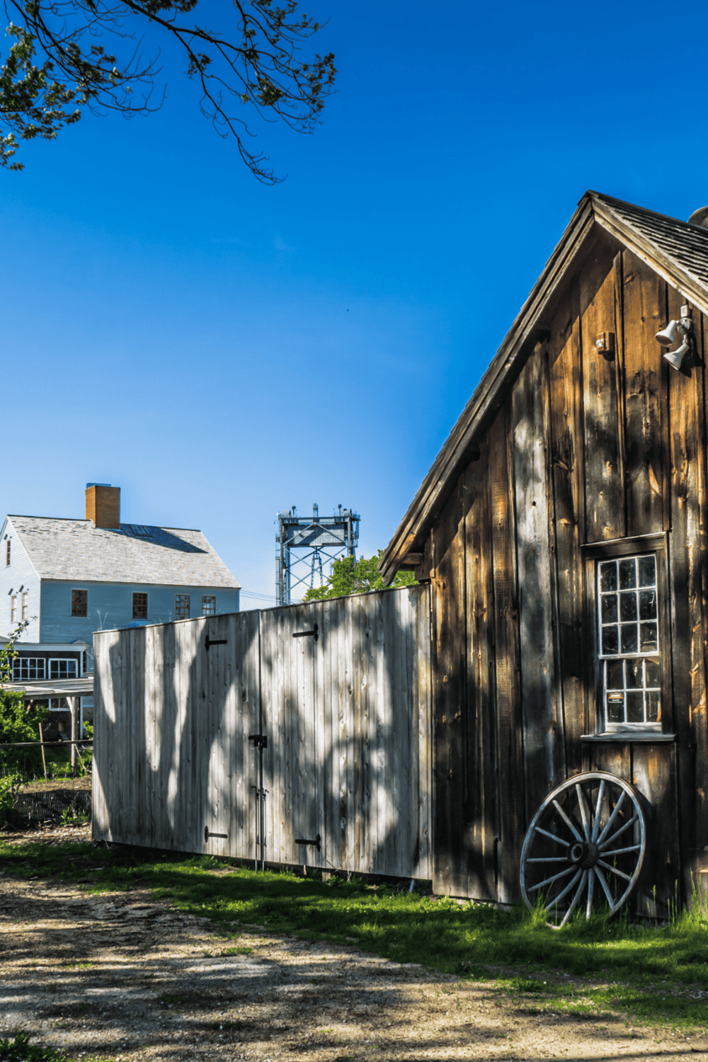 Weathered rustic barn with wooden wagon wheel and classic farm structure under bright blue sky.
