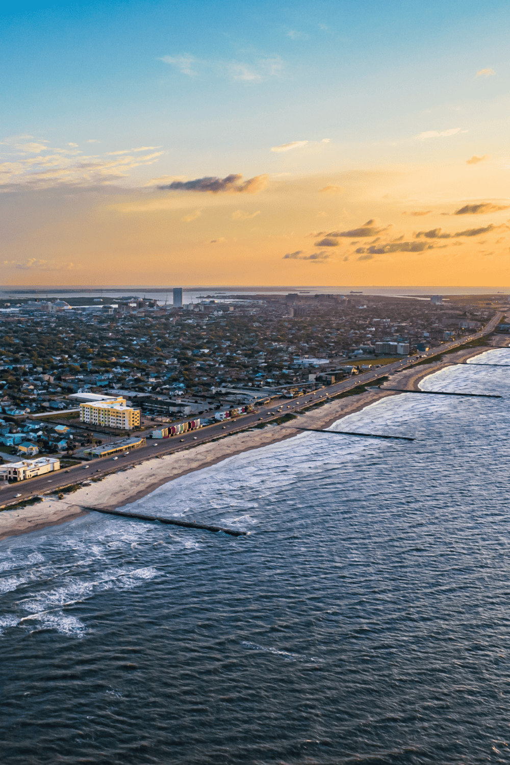 Aerial view of coastal city skyline at sunset, scenic oceanfront with beaches and urban landscape.