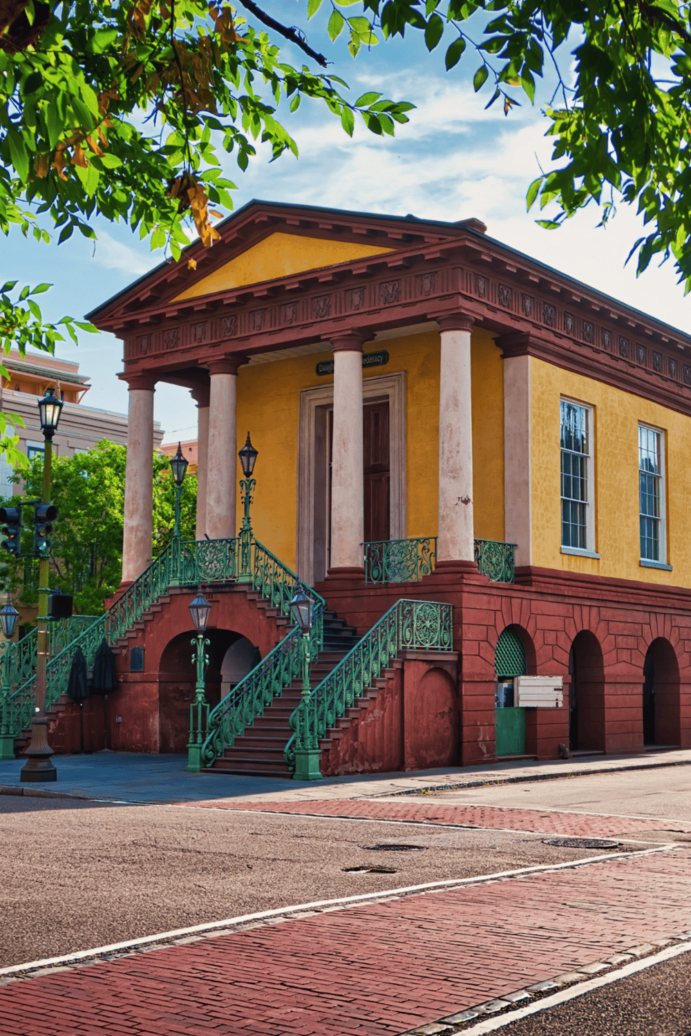 Historic building with classical architecture, yellow facade, columns, and decorative staircase, in a charming city neighborhood.