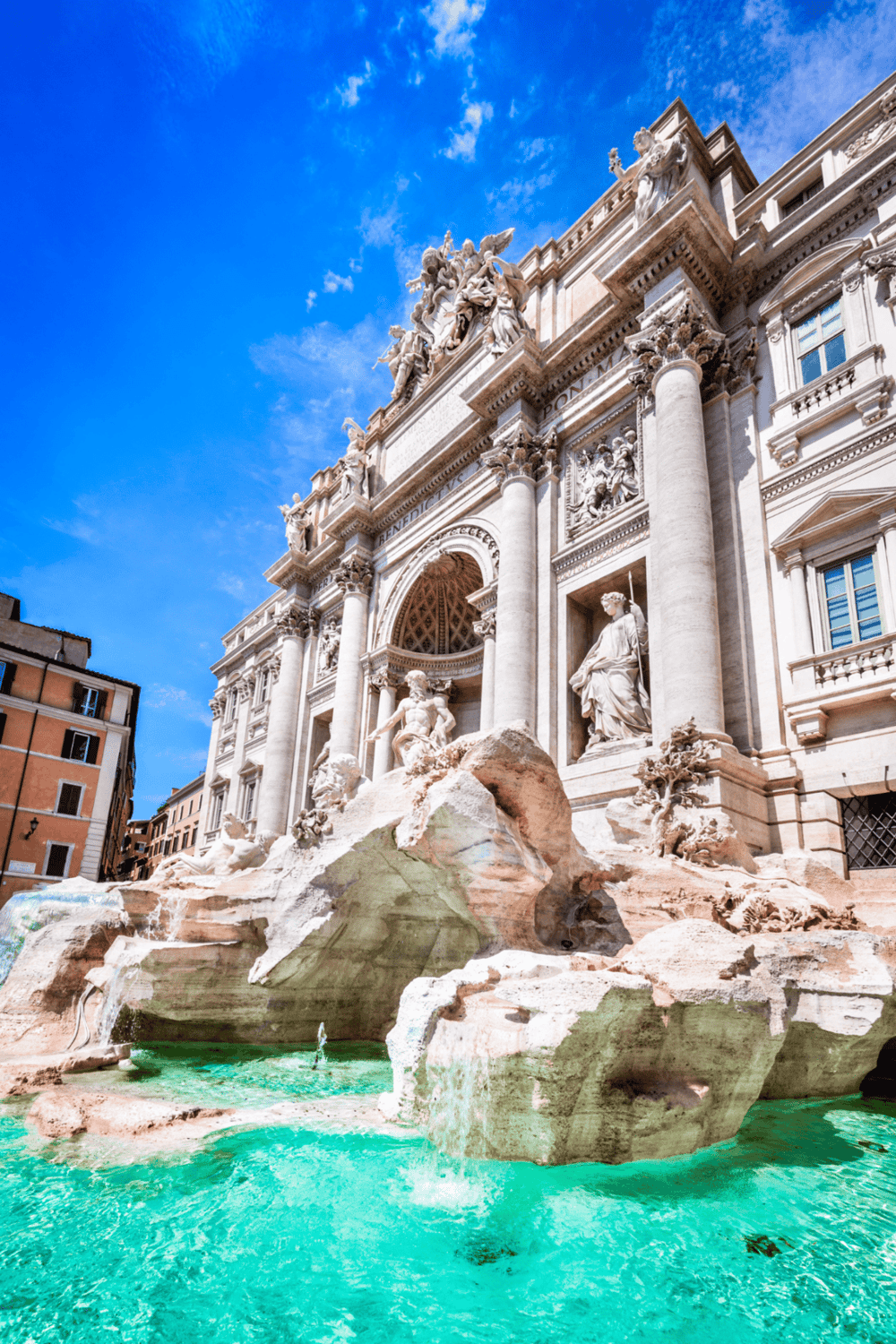 Ancient Roman architecture of Trevi Fountain in Rome, Italy, under a bright blue sky.