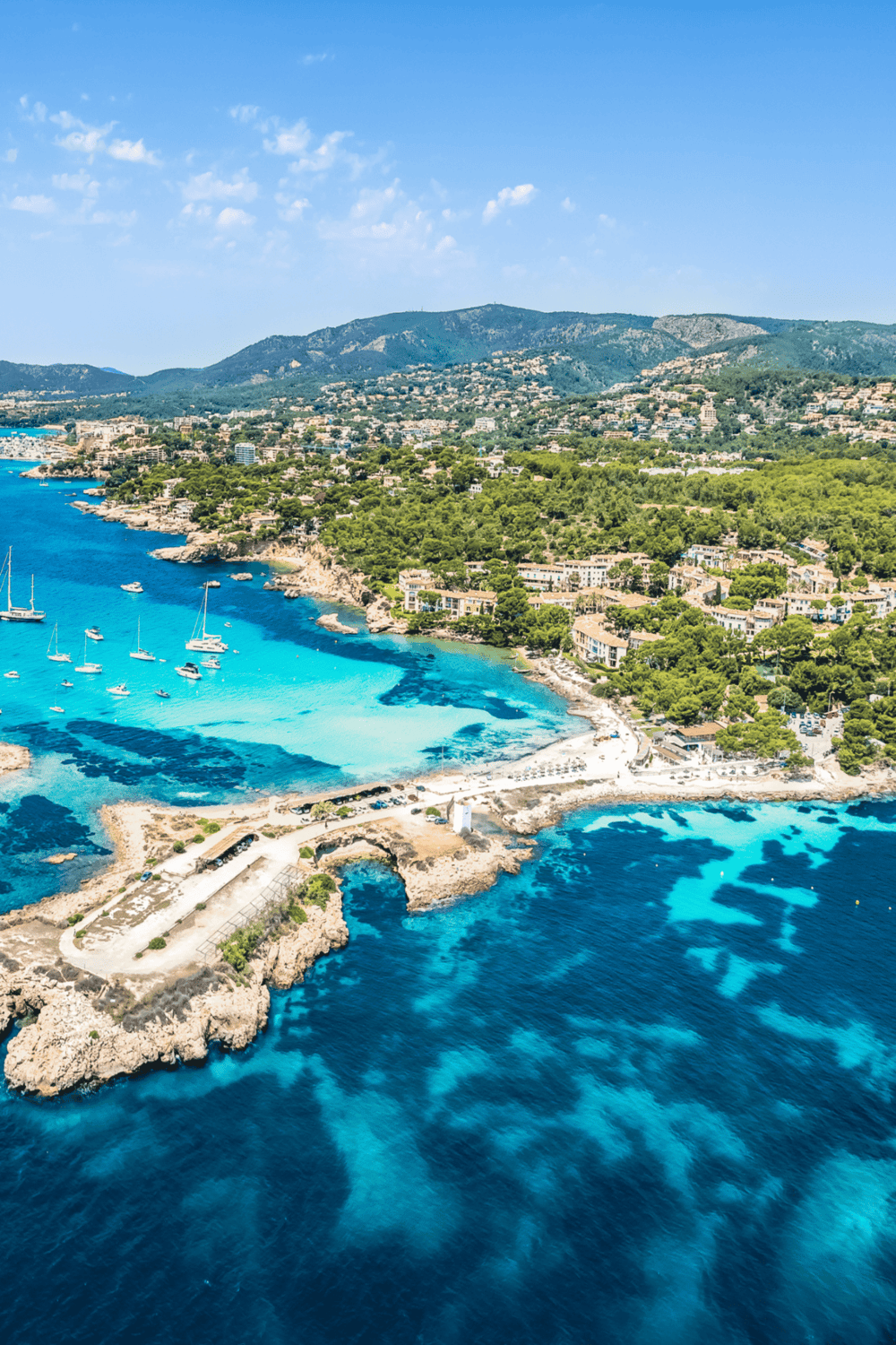Vibrant aerial view of a coastal city with turquoise waters, lush greenery, and scenic mountains in the background.