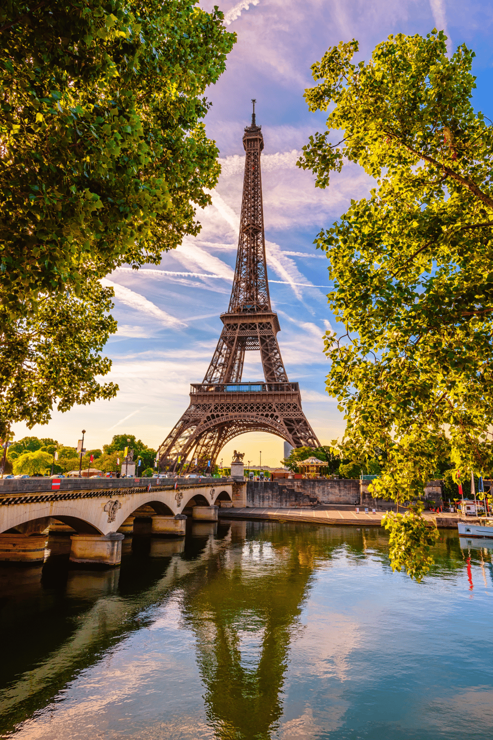 Eiffel Tower in Paris with river and trees, stunning sunset view, iconic Parisian landmark.