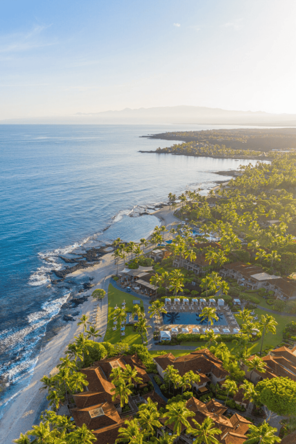 Aerial view of a tropical oceanfront resort with palm trees, outdoor pools, and sandy beaches on a sunny day.