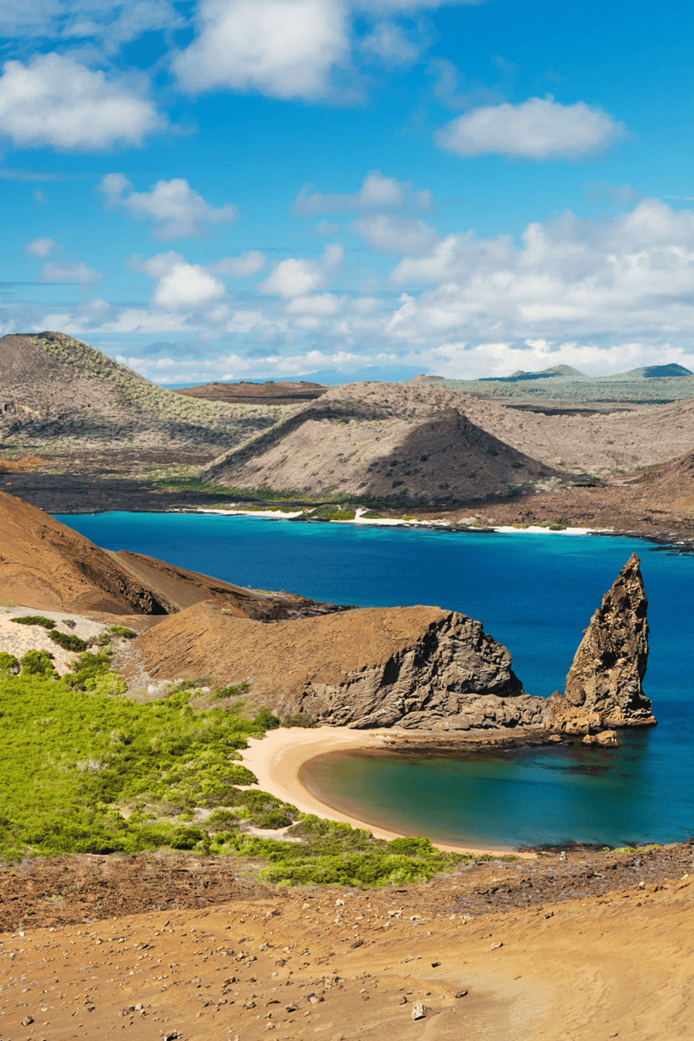 Breathtaking coastal landscape with rocky formations, vibrant blue ocean, and green shoreline under a partly cloudy sky.