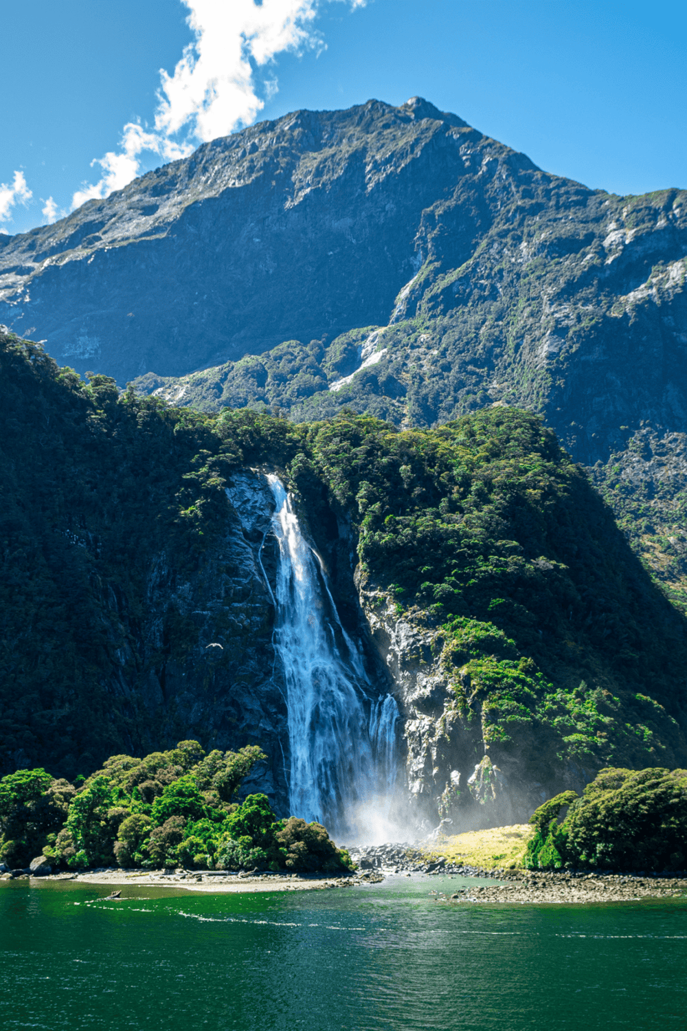 1. Waterfall cascading down lush green mountains with blue sky in background.