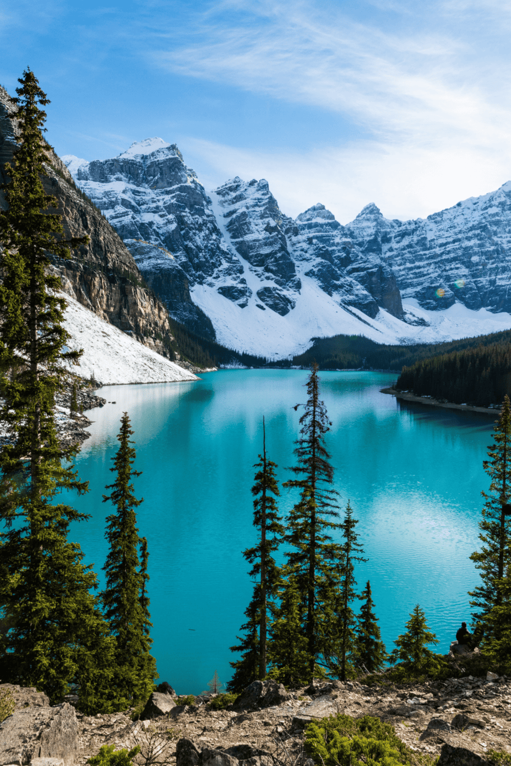 Serene mountain lake with snow-capped peaks, lush pine trees, and vibrant turquoise water, perfect for nature travel and adventure.