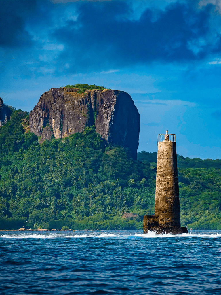 Cliffs and lighthouse at the coast with lush green hills and rocky formations in the background.