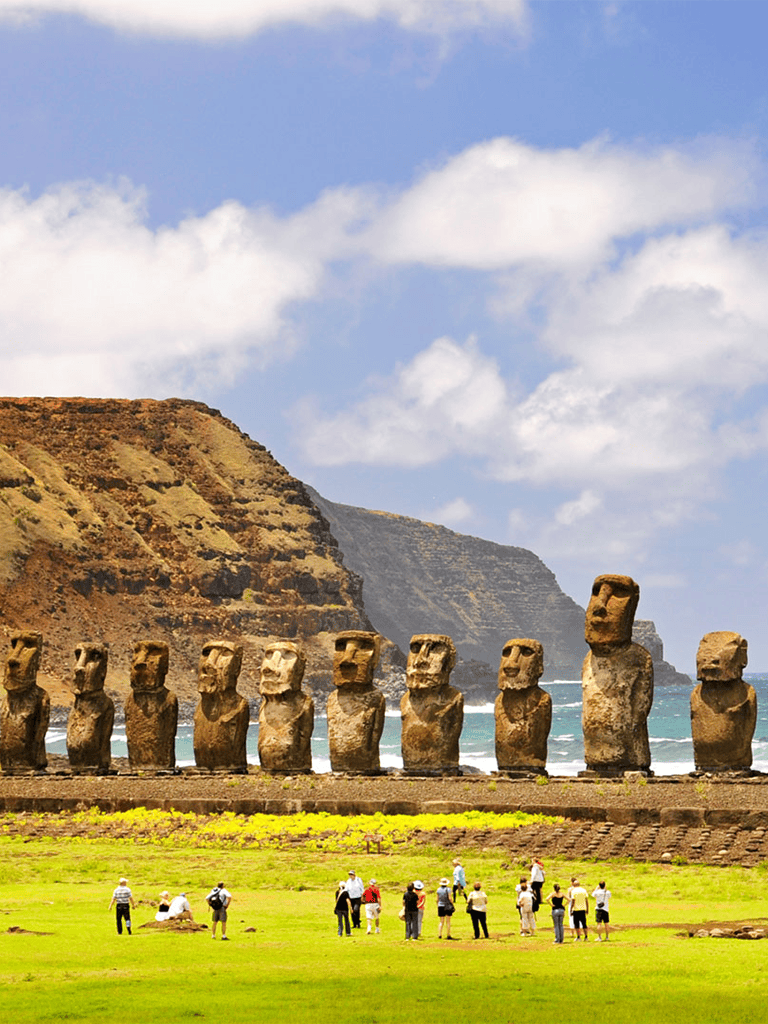 Ancient Moai statues on Easter Island with tourists, scenic coastal background, cultural travel destination.