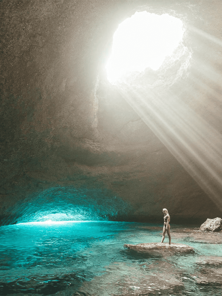 Bright sunlight beams into underground cave with turquoise water, creating a stunning natural scene.