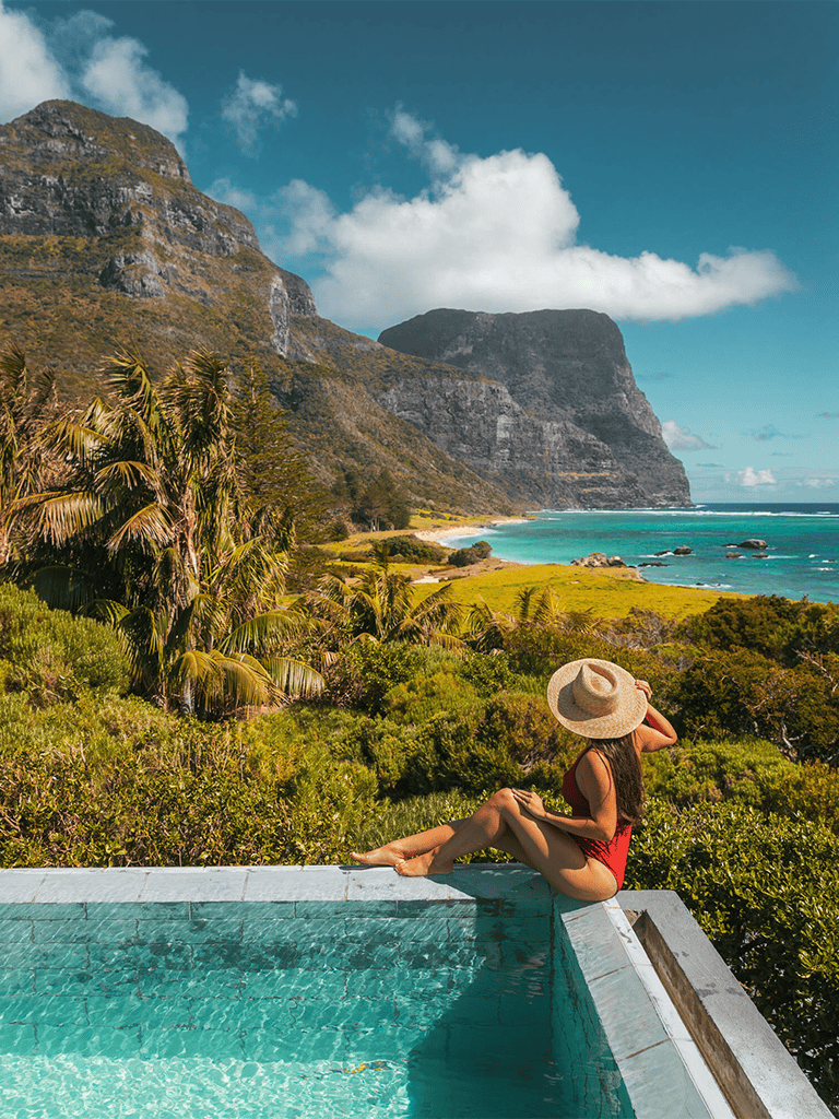 Breathtaking tropical mountain and ocean view with woman relaxing poolside.
